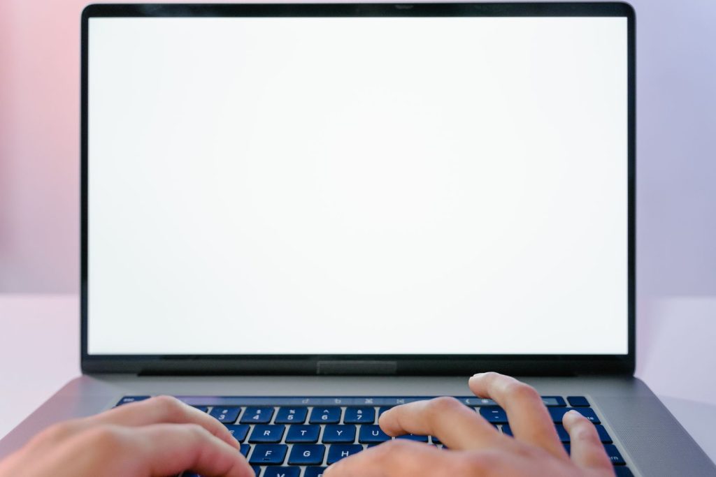 Manos escribiendo en un portátil con pantalla en blanco